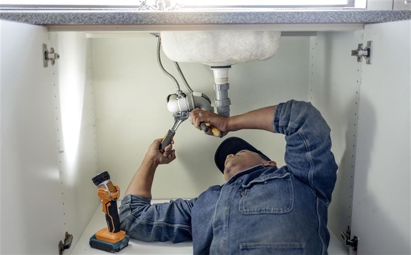Plumber repairing pipes beneath a bathroom sink in Rockledge