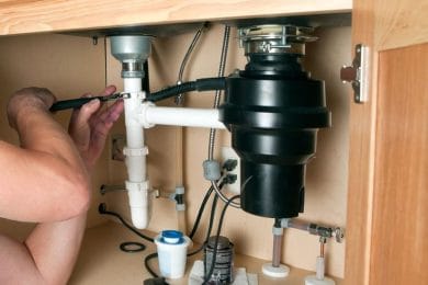 Plumber repairing a garbage disposal beneath a kitchen sink in Rockledge